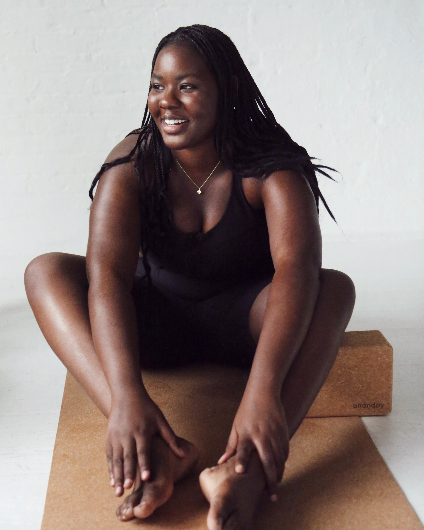 Person seated on an Ananday cork yoga mat with a matching cork yoga block, highlighting the natural cork surface, eco-friendly materials, and comfortable support for yoga, stretching, and meditation.