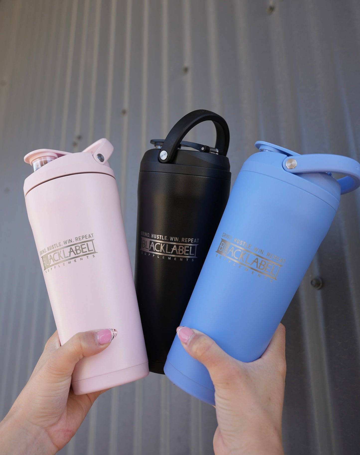 Three BLACKLABEL 24 oz insulated shaker bottles in pink, black, and blue with built-in carry handles, displayed together for color comparison and everyday hydration.