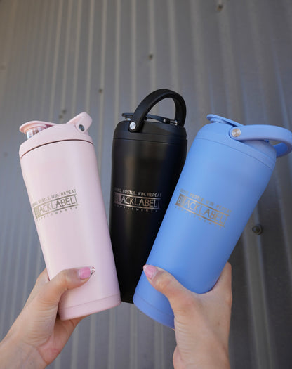 Three BLACKLABEL 24 oz insulated shaker bottles in pink, black, and blue with built-in carry handles, displayed together for color comparison and everyday hydration.