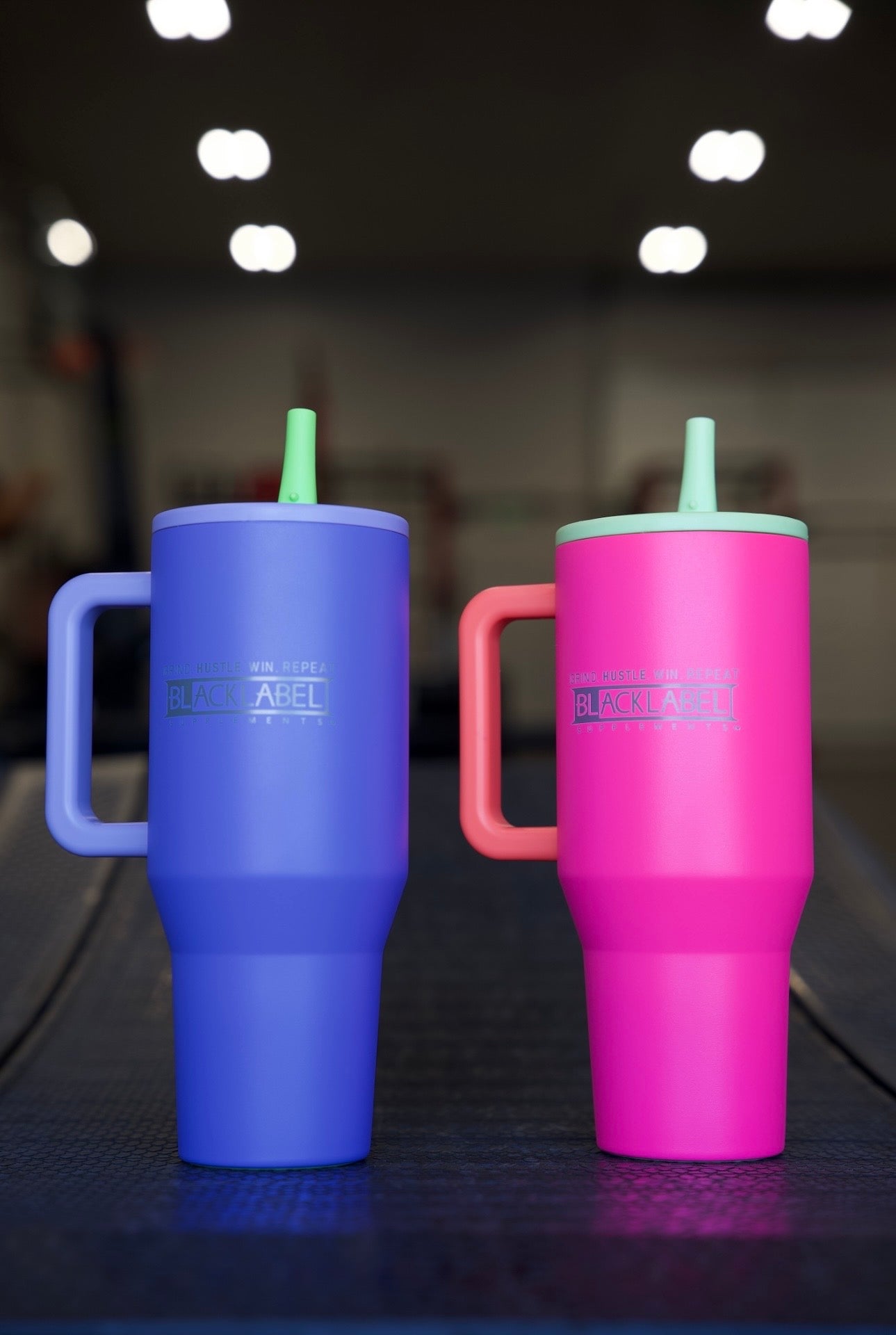 Purple and pink BLACKLABEL 40 oz insulated traveler tumblers with handles and straws displayed side by side, featuring durable matte finishes for hydration at the gym, work, or on the go.