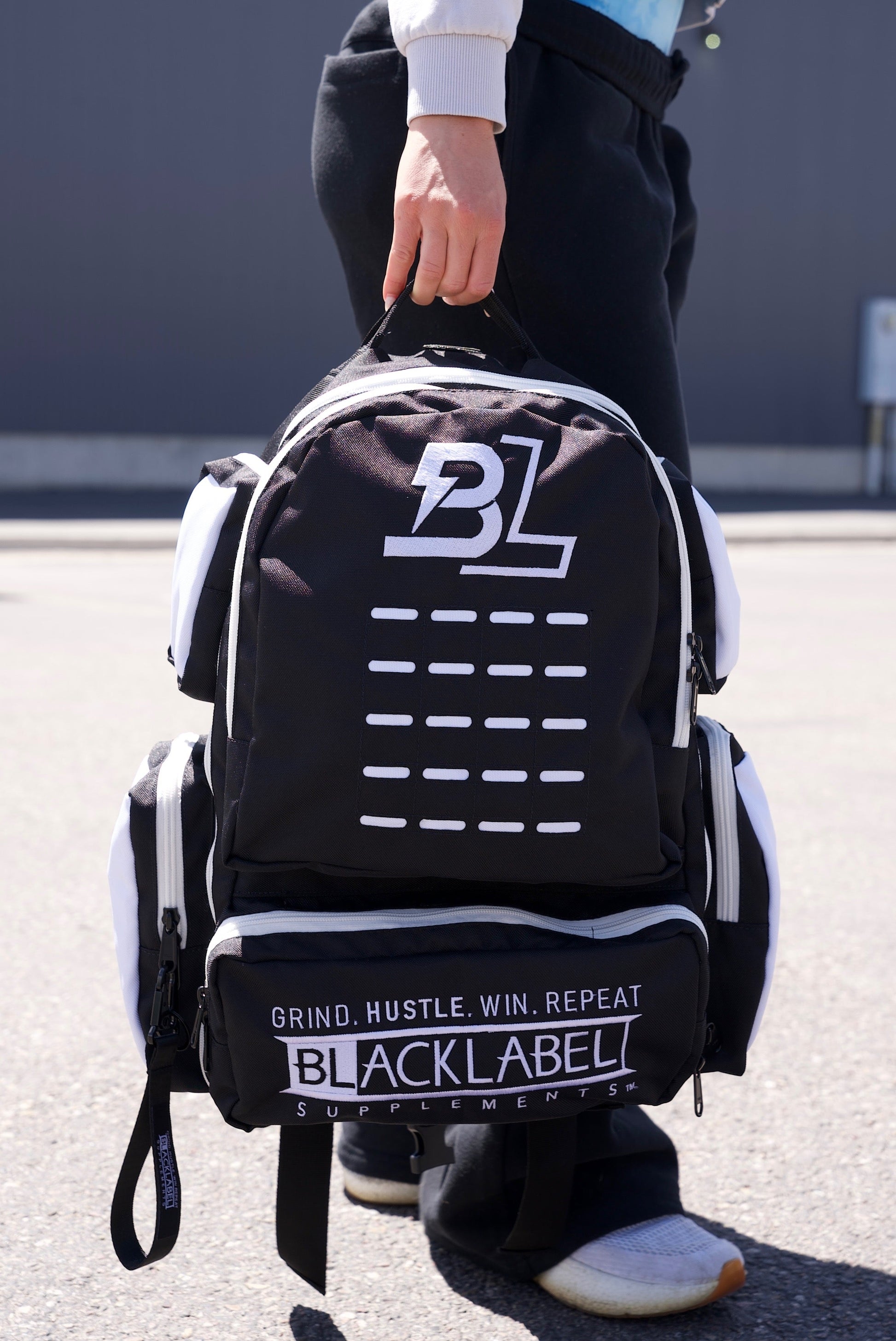 erson carrying the BlackLabel 26L tactical backpack by its top handle outdoors, showcasing the durable gym, travel, and everyday carry backpack with multiple storage compartments.