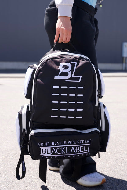 erson carrying the BlackLabel 26L tactical backpack by its top handle outdoors, showcasing the durable gym, travel, and everyday carry backpack with multiple storage compartments.