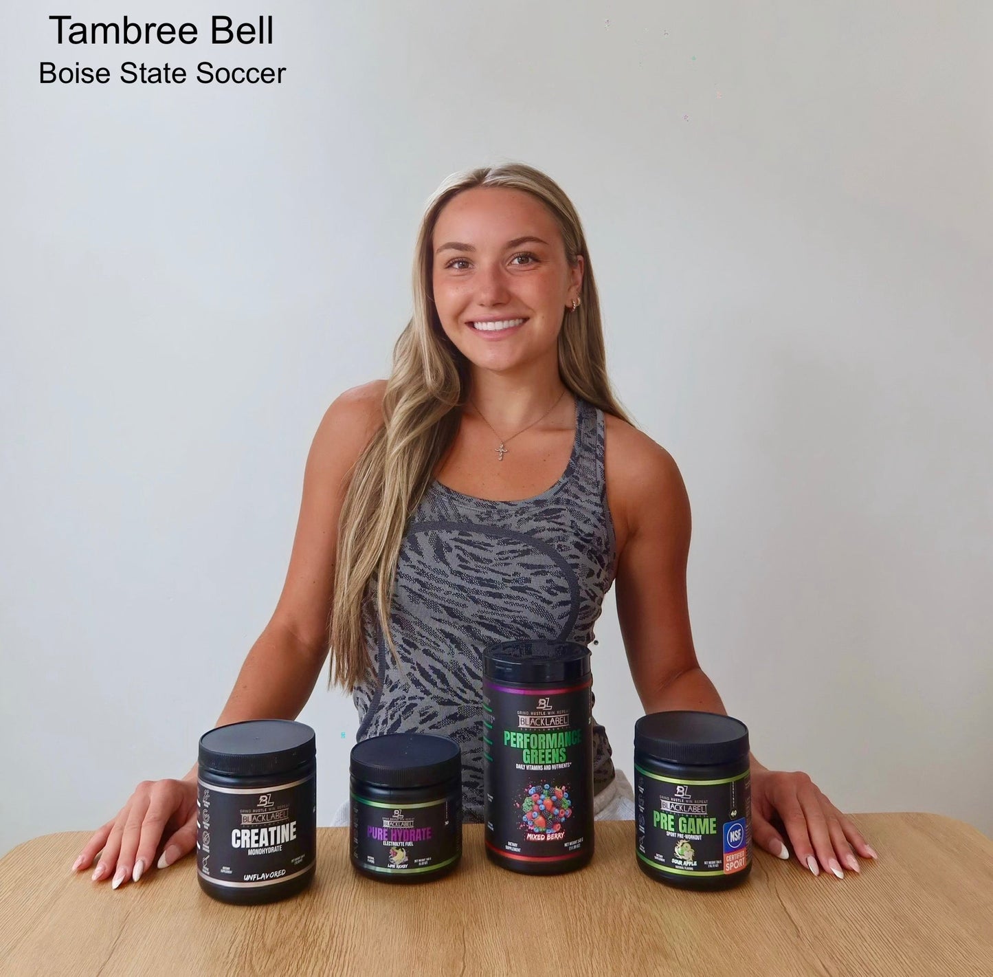 BlackLabel Sports ambassador Tambree Bell of Boise State Soccer posing behind a display of Performance Greens, Pre Game, Pure Hydrate, and Creatine supplements on a wooden table.
