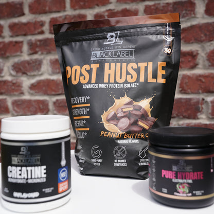 BlackLabel post-workout recovery supplements displayed on a white surface in front of a brick wall, featuring Post Hustle whey protein isolate, Creatine Monohydrate, and Pure Hydrate electrolyte drink mix to support muscle recovery, hydration, strength, and performance.