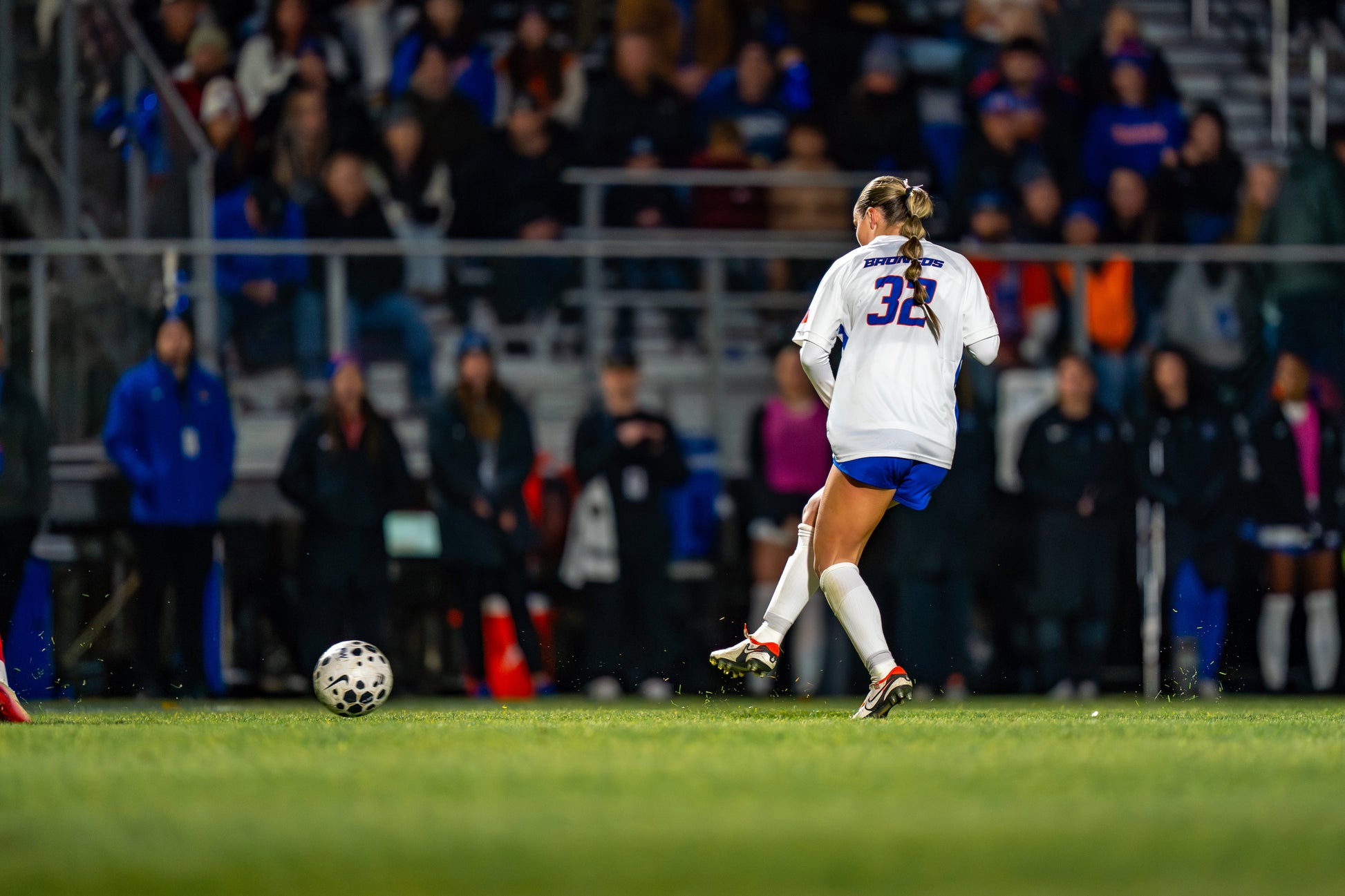 Boise State women's soccer player wearing jersey number 32 chasing the ball during a night match with spectators watching from the stadium stands in the background.