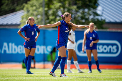 Boise State women's soccer player directing teammates during a match, with players from both teams visible on the field in the background.