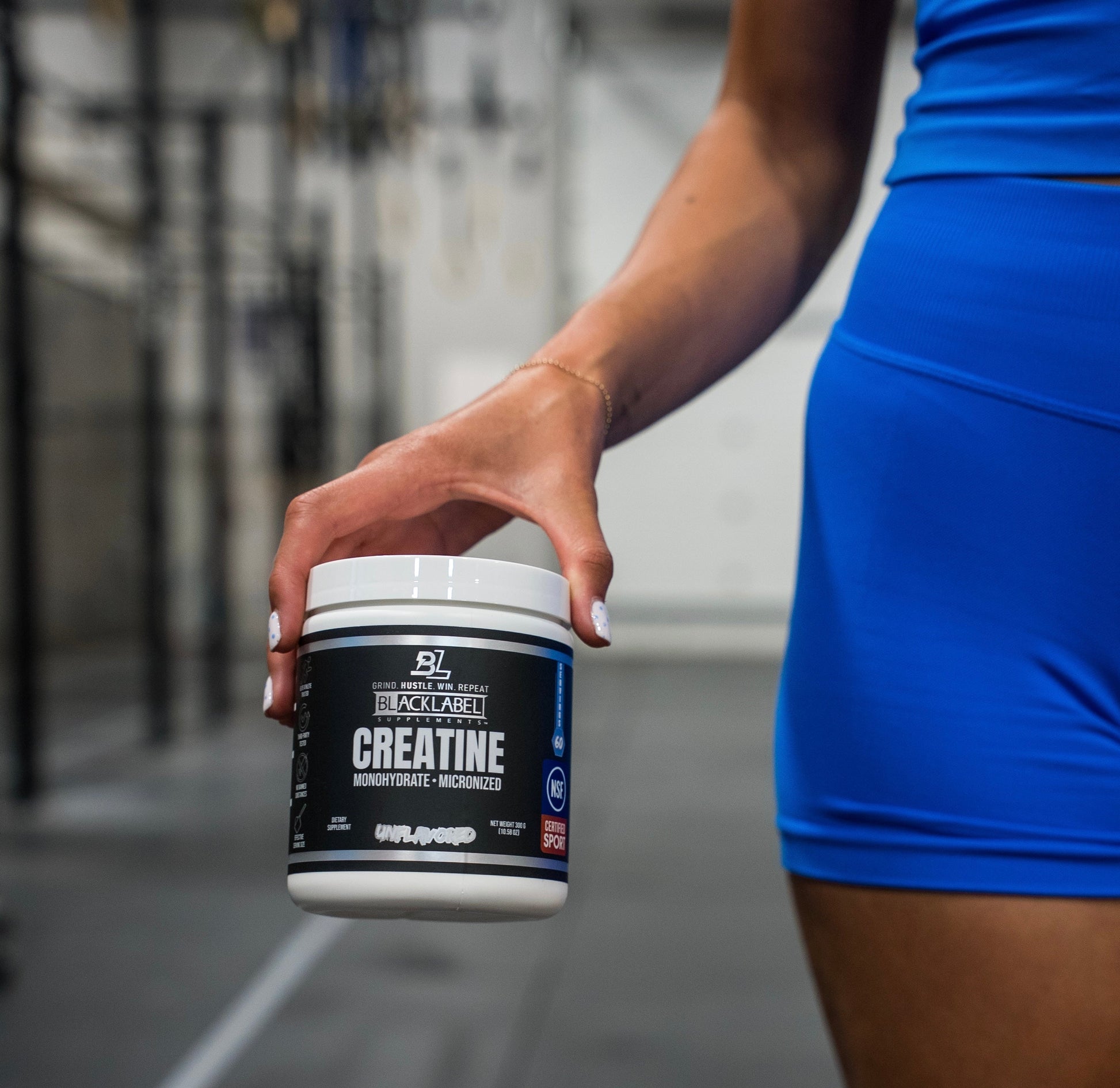 Person holding a container of creatine supplement with a blurred gym background