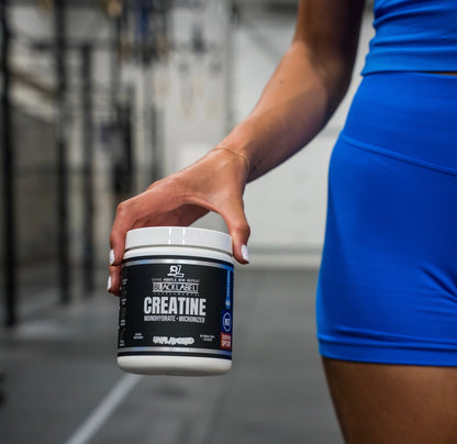 Person holding a container of creatine supplement with a blurred gym background