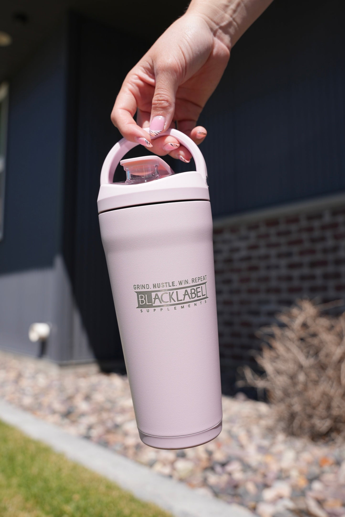 Person carrying a light pink BLACKLABEL 24 oz insulated stainless steel shaker bottle with a built-in handle, ideal for protein shakes, hydration, workouts, commuting, and everyday use.