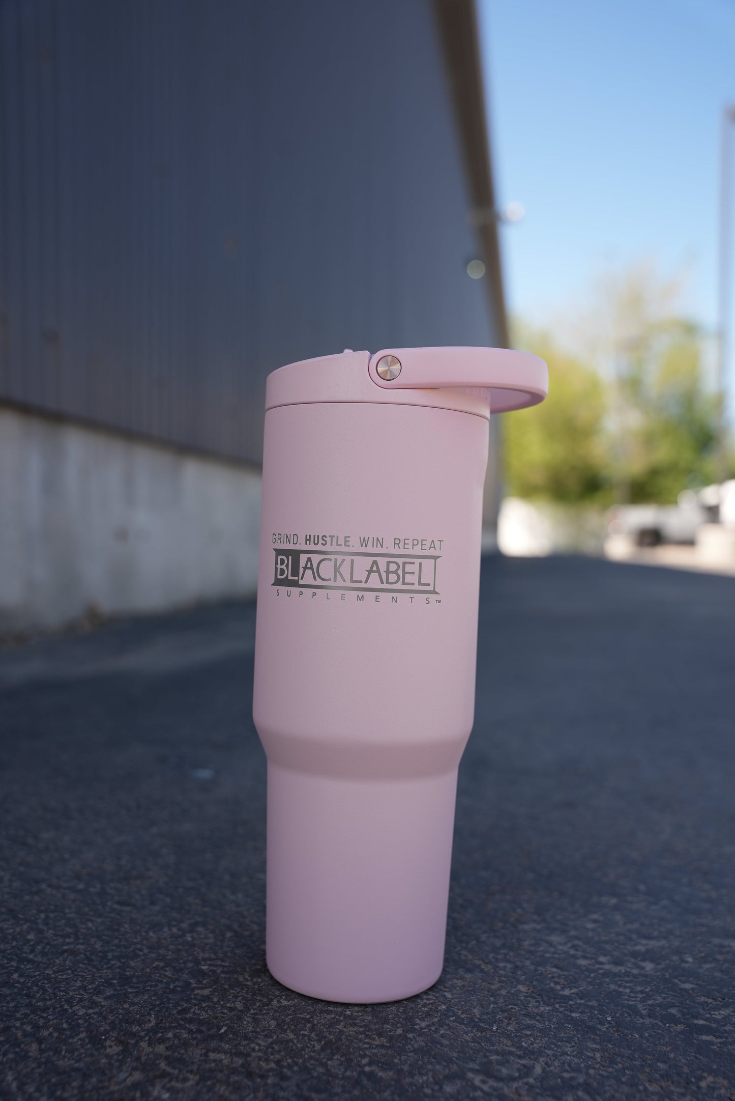 Light pink BLACKLABEL 32 oz insulated sport cup with flip straw lid standing on pavement outdoors, featuring a sleek matte finish for everyday hydration, commuting, workouts, and travel.