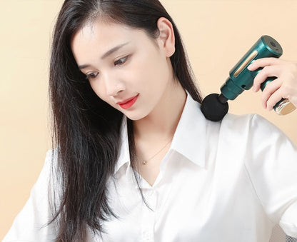 Person using a green cordless percussion massage gun with a round massage head on the neck and shoulder area, demonstrating portable muscle massage for everyday relaxation and post-workout recovery.