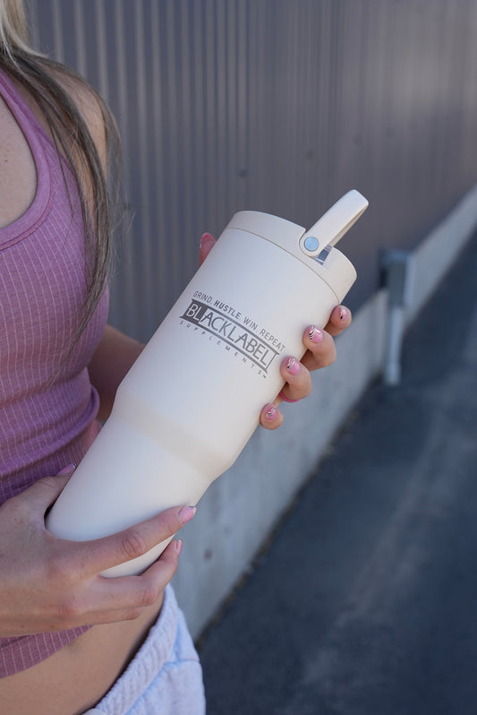 Person holding a white BLACKLABEL 32 oz insulated sport cup with flip straw and leak-resistant lid, designed for convenient hydration during workouts, travel, and everyday use.