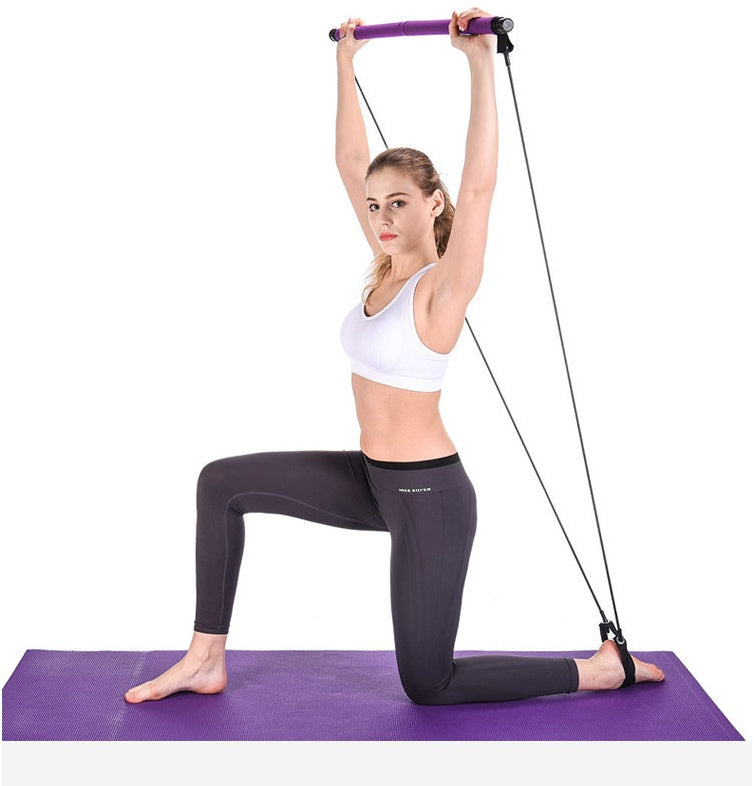 Woman performing an overhead shoulder exercise with a portable Pilates bar resistance band training kit while kneeling on a yoga mat during a full-body home workout.