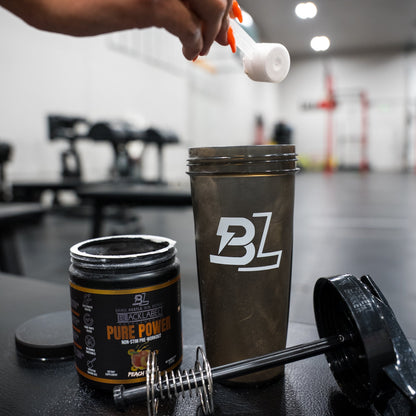 Person adding powder to a shaker bottle with BZ logo in a gym setting